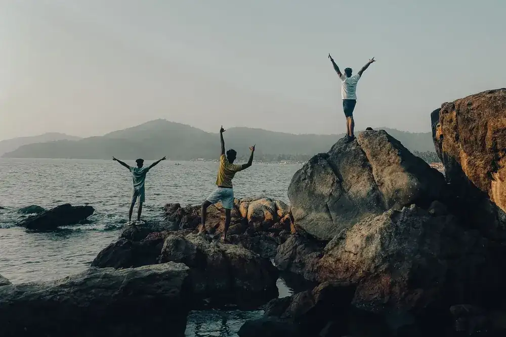 Friends sitting arm in arm on a wall, looking out at the sea