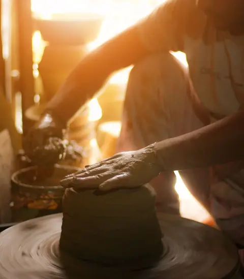 A potter shaping clay on a wheel in a sunlit Indian workshop