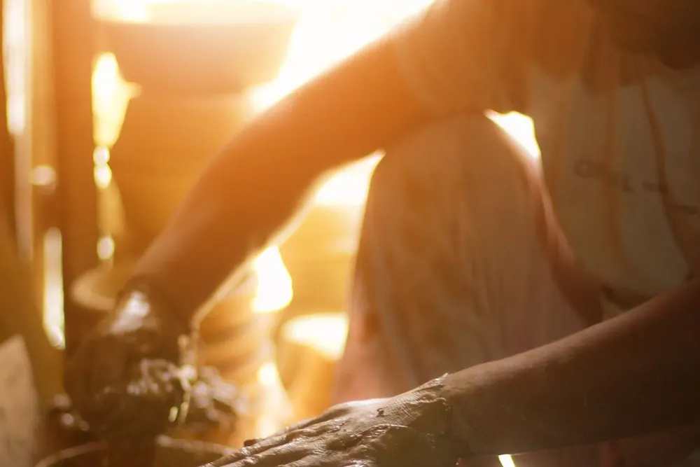A potter working at a clay wheel in a sunlit Delhi studio