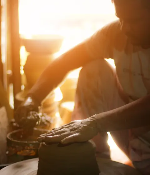 A potter shaping clay on a wheel in a sunlit Delhi workshop